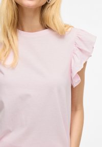 Helles rosa Kurzarmoberteil mit rüschierten Schulterakzenten und einem Rundhalsausschnitt, aus weichem Stoff mit glatter Textur gefertigt.