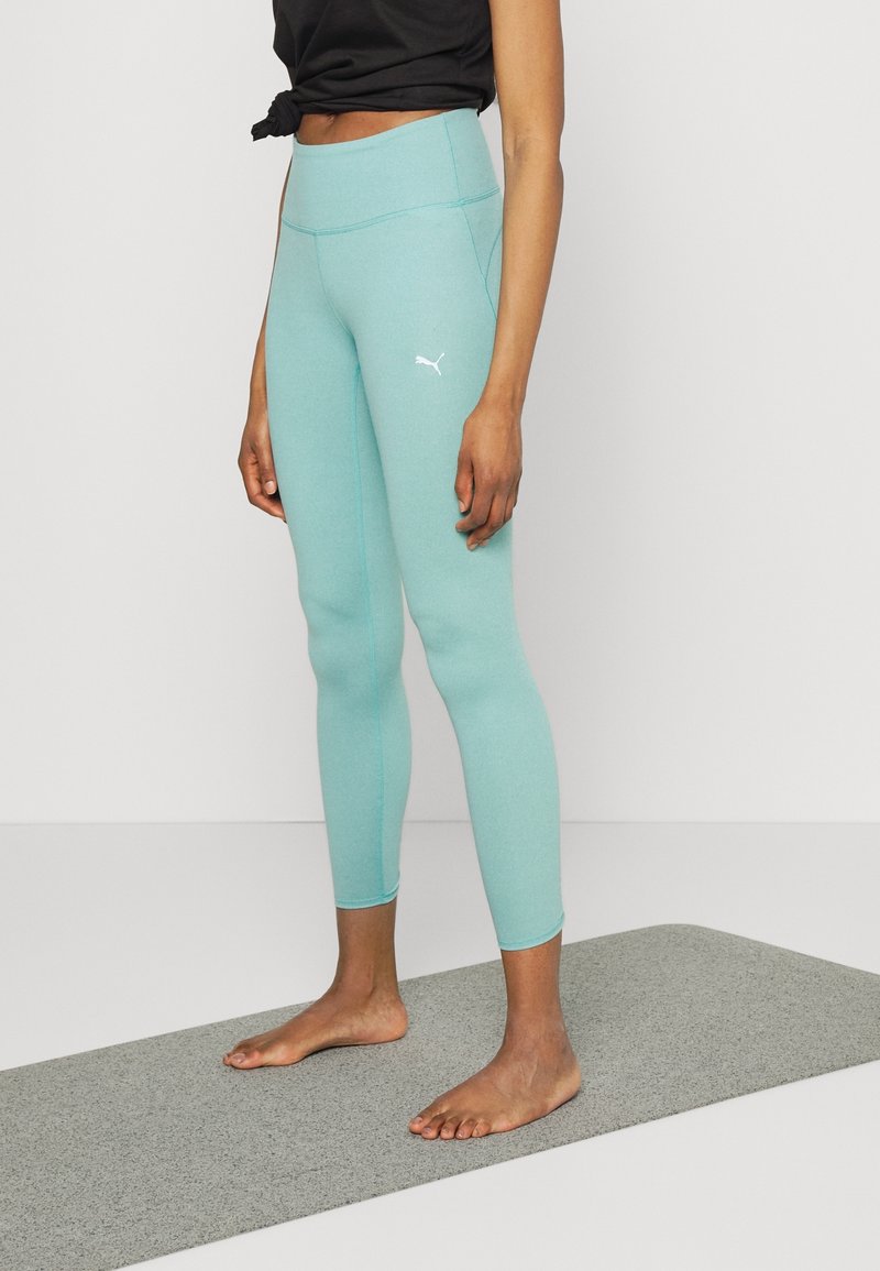 Ljus teal leggings i stretchmaterial, med hög midja och en liten vit logotyp på sidan. Slät textur och åtsittande design.