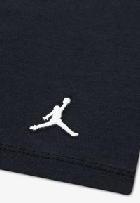 Tissu en coton noir à texture lisse, avec un logo Jumpman blanc brodé dans le coin inférieur. Design simple sans motifs.