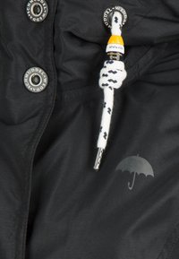 Chaqueta negra impermeable con broches de metal, un cordón blanco y azul marino con una punta de metal, y un sutil logo de paraguas gris en la tela.