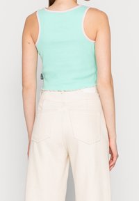 Mintgrön ribbad crop top med rosa kant, med en scalloped nederkant. Kombinerad med krämfärgade vida byxor med bakfickor.