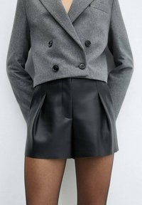 Blazer de lana gris cruzado con botones negros, combinado con shorts de cuero negro de talle alto con pliegues frontales y textura suave.