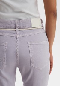 Jeans di denim lilla con un'etichetta in pelle bianca in vita e un accento in corda beige, caratterizzati da due tasche posteriori con alette angolate.
