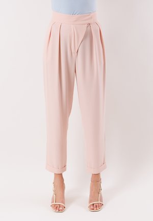 Pantaloni rosa chiaro a vita alta, a gamba affusolata con pieghe e orli risvoltati, abbinati a sandali nude con cinturini e tacchi alti su sfondo bianco.