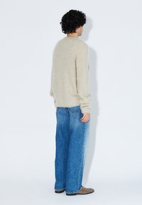 Hellbeiger Strickpullover mit strukturierter Oberfläche, kombiniert mit weiten blauen Denim-Jeans. Das Outfit hat eine lockere Passform.