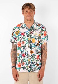 Chemise à manches courtes avec un fond rose pastel et un motif floral dense de couleurs variées. Devant à boutons et détail de poche poitrine.