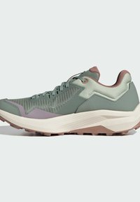 Baskets de trail vert clair avec un matériau en mesh et synthétique, présentant un dessus texturé, des accents rosés, une semelle intermédiaire blanche épaisse et une semelle extérieure marron.