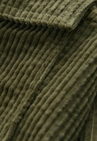 Olivgrüner Cordstoff mit erhabener Ripptextur, der parallel verlaufende Rillen und eine weiche Oberfläche aufweist. Geeignet für Bekleidung oder Polsterungen.