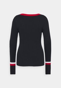 Pull noir à manches longues côtelé avec bordure de col rouge et rayures rouges et blanches sur les poignets des manches, vu de dos sur un fond uni.