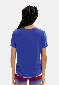 Bawełniana koszulka w jednolitym królewskim niebieskim kolorze, z krótkimi rękawami i okrągłym dekoltem, zestawiona z szortami w czerwono-niebieskie paski widocznymi na dole.