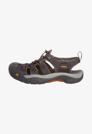 Sandalia deportiva con un upper de textil azul marino de diseño abierto, suela de goma gris, detalles en naranja y cordón ajustable para un ajuste seguro.