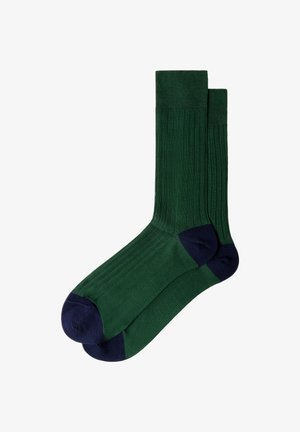 Een paar donker groene geribbelde sokken met marineblauwe teen- en hielgedeelten, vlak gelegd en overlappend op een witte achtergrond.
