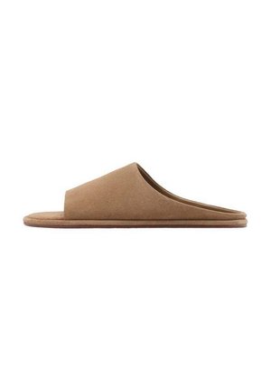 Zapatilla marrón de ante con puntera abierta, de tipo slip-on, con suela plana y diseño minimalista, mostrada en vista lateral sobre fondo blanco.