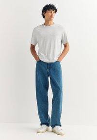 Camiseta de algodón gris, corte relajado, mangas cortas, combinada con vaqueros azules, corte holgado, usada con zapatillas blancas. Diseño sencillo y casual.