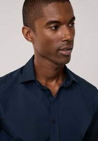 Camisa azul marino de botones con cuello clásico, textura suave y botones oscuros. Presenta un brillo sutil y un ajuste estructurado.