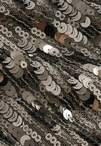 Gros plan de sequins argentés et métalliques cousus densément sur un tissu foncé, formant des rangées et chaînes scintillantes qui se chevauchent.