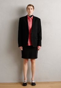 Schwarzes maßgeschneidertes Blazer über einem rosa Hemd mit Knöpfen, kombiniert mit einem schwarzen Rock und schwarzen Schuhen mit weißen Akzenten. Minimalistisches Design.