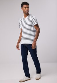 Raidallinen lyhythihainen paita musta-valkoisena, yhdistetty tummansinisisiin farkkuihin ja valkoisiin tennareihin ruskeilla yksityiskohdilla, esittelee rentoa ilmettä.