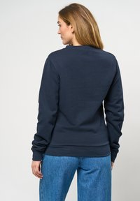 Námorně modrý svetr s dlouhým rukávem a kulatým výstřihem, s žebrovanými manžetami a texturovanou tkaninou. Nosit s světle modrými džíny.