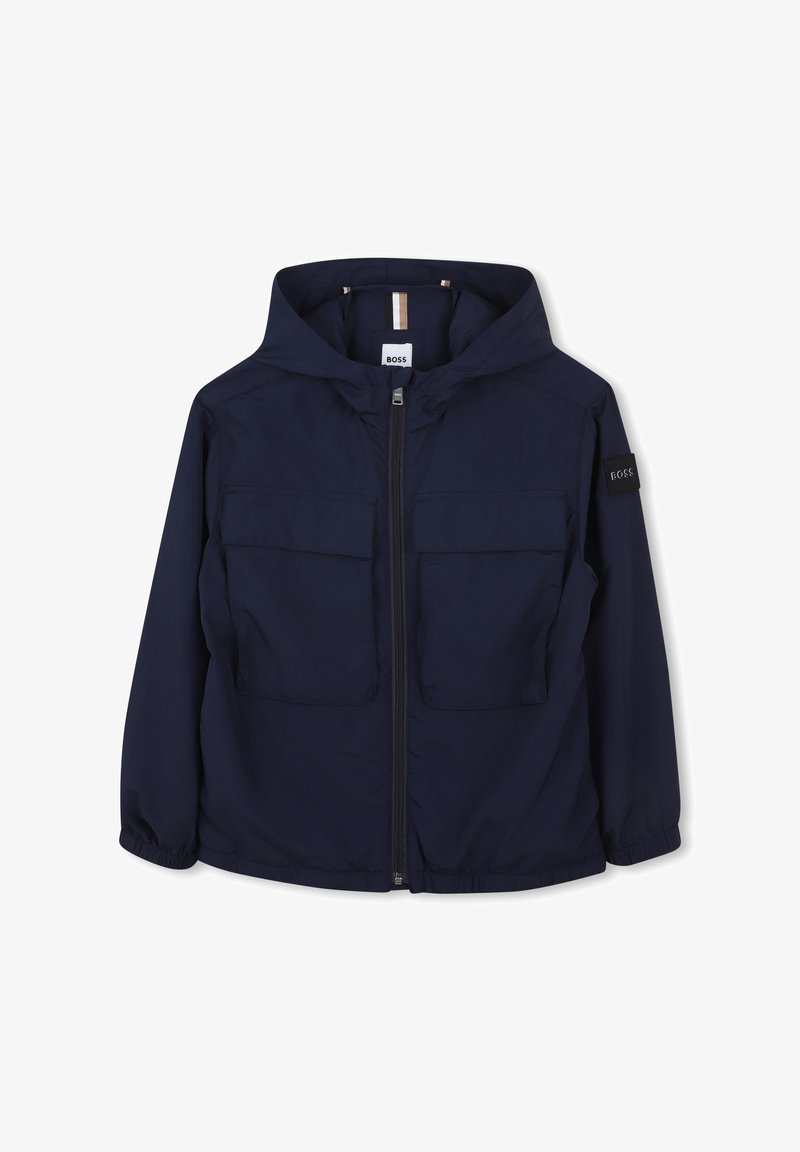 Giacca a vento blu navy con cappuccio, chiusura con zip e due tasche frontali. Presenta un patch con logo sulla manica sinistra e polsini elasticizzati.