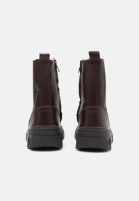Botas de tobillo de cuero marrón con acabado texturizado, que cuentan con un cierre de cremallera, suelas de goma y detalles en negro contrastantes.