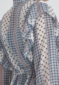 Abito in tessuto leggero con un motivo geometrico blu, bianco e rosa; presenta maniche arricciate e una vita con cintura.