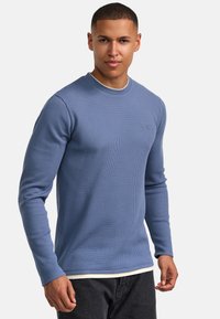 Langarmtrui met geribbelde ronde hals in lichtblauw. Heeft een gestructureerde weefsel, slim fit en een subtiel logo op de borst.