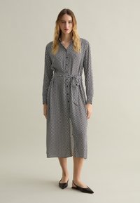 Black and white polka dot dress with button front, long sleeves, cinched waist, and ankle-length hem. Paired with black flat shoes.