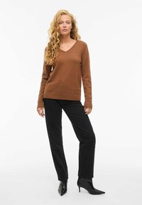 Rudas v-kaklo megztinis, pagamintas iš minkštos medžiagos, derinamas su tiesių kojų juodomis kelnėmis. Modelis vilki juodas aštriais pirštais aukštakulnes. Paprastas, minimalus dizainas.