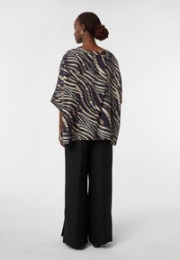 Top fluido con stampa zebra nera e oro, con maniche ampie, abbinato a pantaloni neri a gamba larga, che mettono in risalto una silhouette e una texture rilassate.
