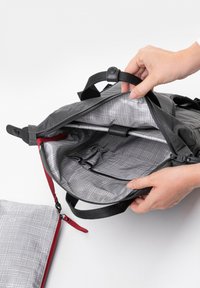 Zaino nero con un interno grigio aperto, caratterizzato da un motivo a griglia. Include tasche organizzative e una rifinitura con cerniera rossa.
