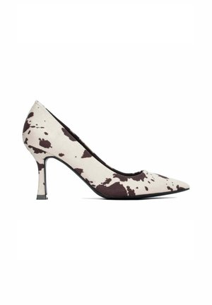 Zapato de tacón alto con punta puntiaguda, base blanca y patrón irregular de estampado de vaca marrón oscuro, presentado sobre fondo blanco liso.