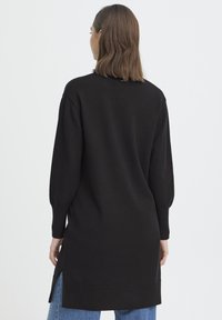 Fekete kötött pulóver hosszú ujjakkal, bordázott szegéllyel és oldalsó hasítékokkal, laza szabással és díszítések nélküli minimalista kialakítással.