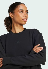 Felpa nera realizzata in morbido tessuto, con scollatura rotonda e maniche lunghe. Logo adidas ben visibile in nero tono su tono sul petto.