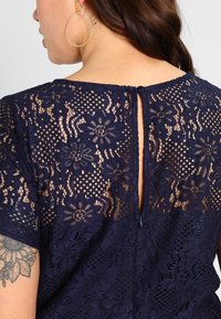 Navy blue lace dress with floral patterns, featuring a keyhole back detail and short sleeves. Textured lace adds depth to the design.