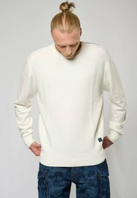 Witte, gestructureerde trui met lange mouwen, voorzien van een geribde halslijn en zijdetails. Gekenmerkt door de combinatie met blauwe cargobroeken.