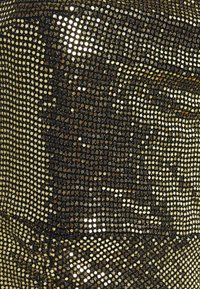 Tissu noir orné de clous dorés ronds, créant une surface texturée et chatoyante. Le motif est cohérent avec des réflexions de lumière variées.