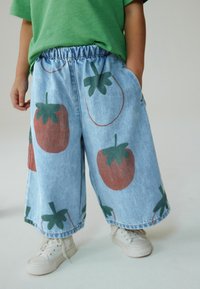 Lyseblå denimshorts med elastisk talje, prydet med store røde og grønne jordbærtryk og sidelommer, kombineret med hvide sneakers.