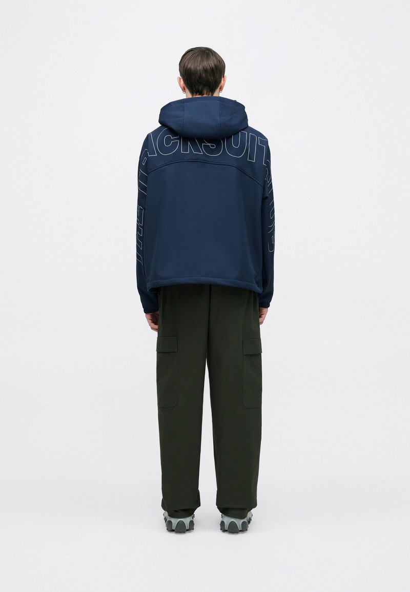 Tengeralattjáró kék kapucnis pulóver nagy grafikával a hátoldalán, olívazöld dzseki nadrággal és szürke tornacipővel párosítva. Hétköznapi, laza fazon.