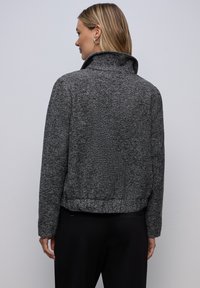 Strukturalna, czarno-biała kurtka z wysokim kołnierzem, skróconym krojem i dopasowanymi rękawami, z delikatnym wzorem w jodełkę.