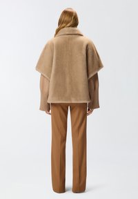 Cardigan beige in misto lana a stile scialle con maniche ampie e una texture morbida, abbinato a pantaloni marroni sartoriali.