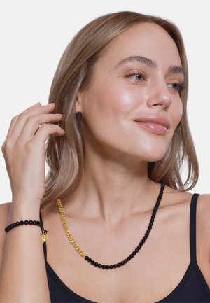 Zwarte kralenketting met een gouden kettingaccent. Gladde, ronde kralen zijn afwisselend geplaatst en creëren een contrast met het metalen kettingdetail.