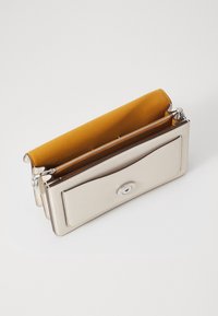 Portefeuille argenté métallique avec un intérieur jaune moutarde, doté d'un compartiment zippé et d'une fermeture à bouton-pression magnétique. Texture lisse, design minimaliste.