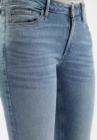 Jasnoniebieskie dżinsy o wąskim kroju, z tradycyjnym pięciopocketowym wzorem, delikatnym wyblaknięciem oraz metalowym zapięciem na zamek.