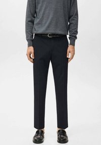 Pantaloni neri su misura con una vestibilità dritta. Realizzati in tessuto leggero, caratterizzati da una trama liscia e da una sottile lucentezza, abbinati a una maglia grigia.