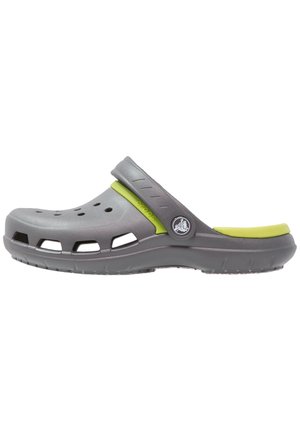 Zueco de plástico gris con una correa verde de acento, que cuenta con múltiples orificios de ventilación, una superficie texturizada y una suela de goma antideslizante.