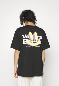 Zwarte katoen T-shirt met een grote multikleurige grafische afbeelding op de achterkant met tekst en een handafdrukontwerp. Losse pasvorm, korte mouwen.