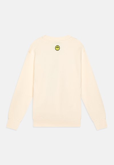 Sudadera crema de manga larga, con puños y dobladillo acanalados. Presenta un pequeño parche de cara sonriente negra y amarilla en la parte posterior del cuello.