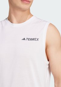 White sleeveless athletic shirt made of a lightweight fabric. Features the "TERREX" logo in black on the chest. Smooth texture.