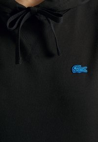 Sweat à capuche noir avec un cordon noué et un petit logo crocodile bleu brodé sur la poitrine.